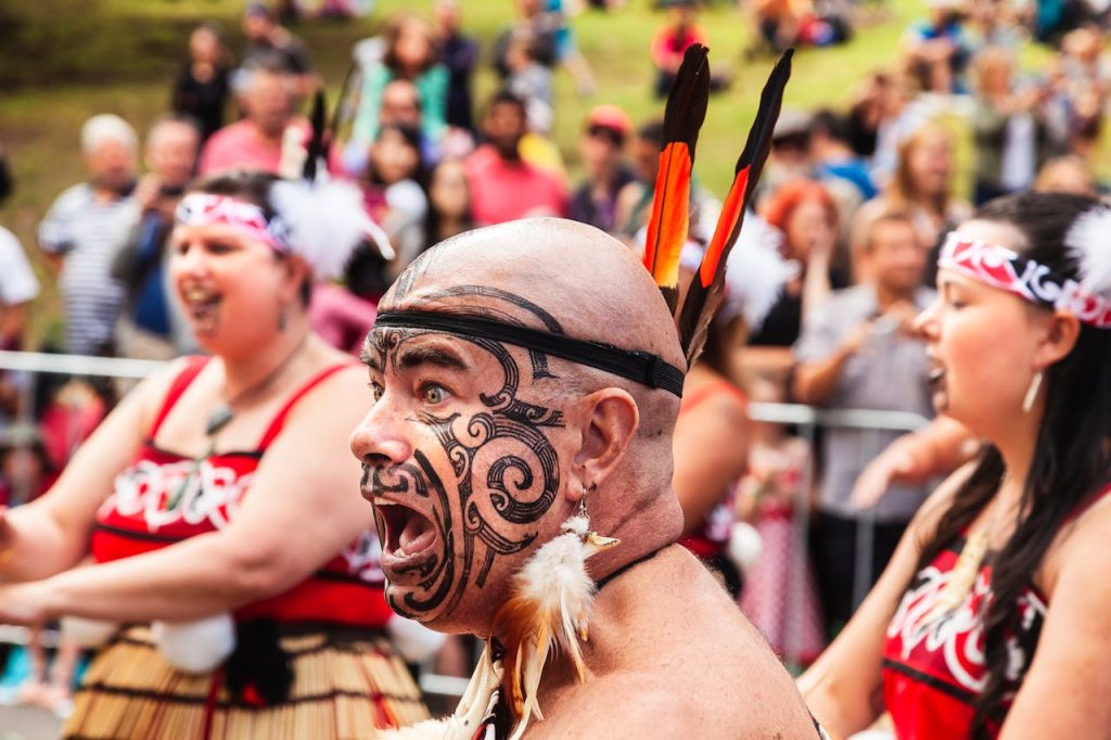 man-with-painted-face-9276647 An energetic Maori performer with a painted face during a tribal festival in daylight.